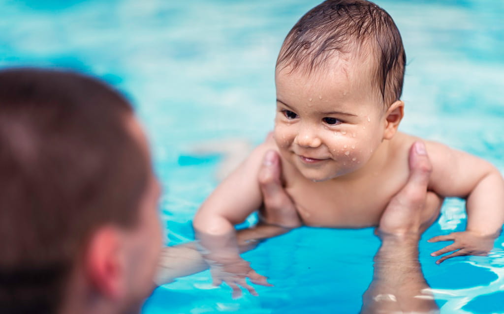 Vater hält Baby im Wasser fest beim Babyschwimmen