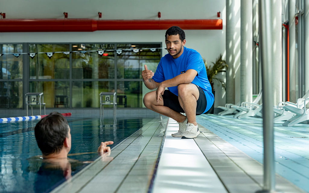 Ein Bad-Mitarbeiter spricht am Beckenrand mit einem Schwimmer