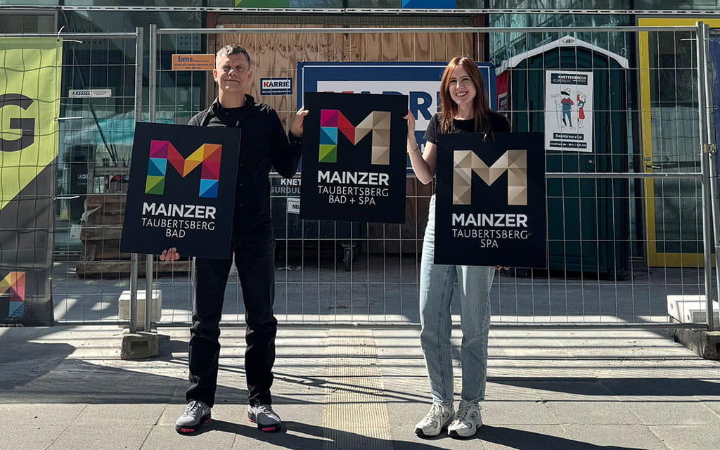 Zwei Personen halten die neuen Logos des Taubertsbergbad und Spas hoch
