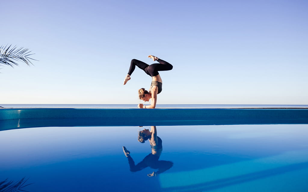 Frau macht Yogaübung über Kopf an einem Schwimmbecken