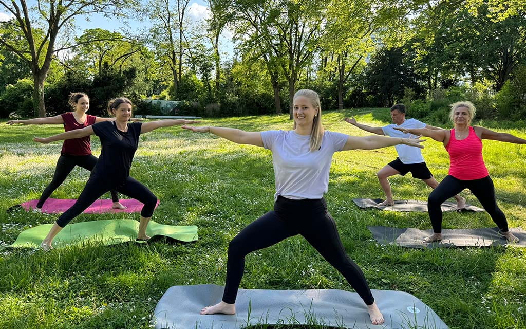 Fünf Personen in Yoga-Position auf der Freibadwiese des Taubertsbergbads