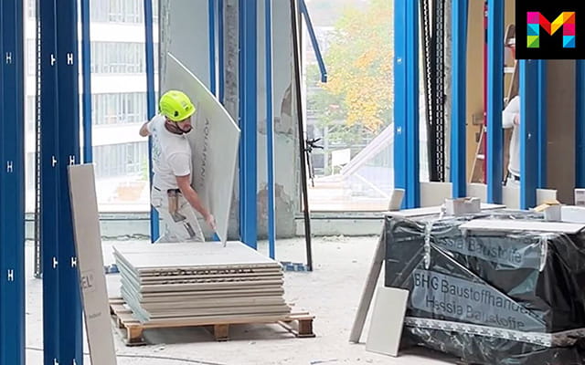 Mann trägt eine Platte über eine Baustelle